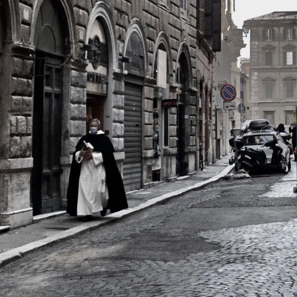 A priest in gown walks through the streets of Rome in color.